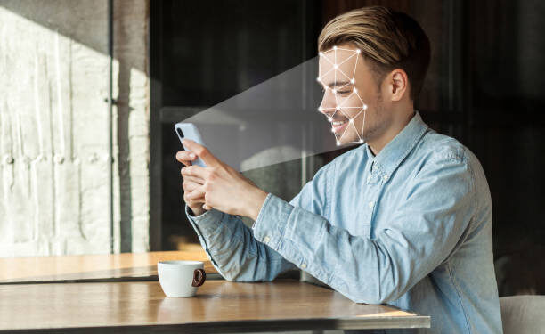 Mobile biometric identification and verification face detection concept. face ID scaning or unlocking technology. young happy man sitting and scanning face with facial recognition system on smartphone