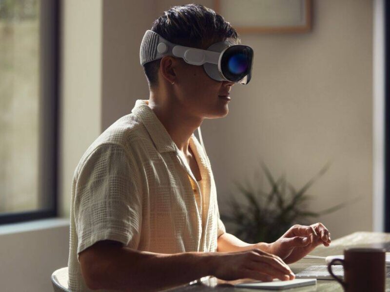 A man wearing an Apple vision pro and sit in front of a desk.