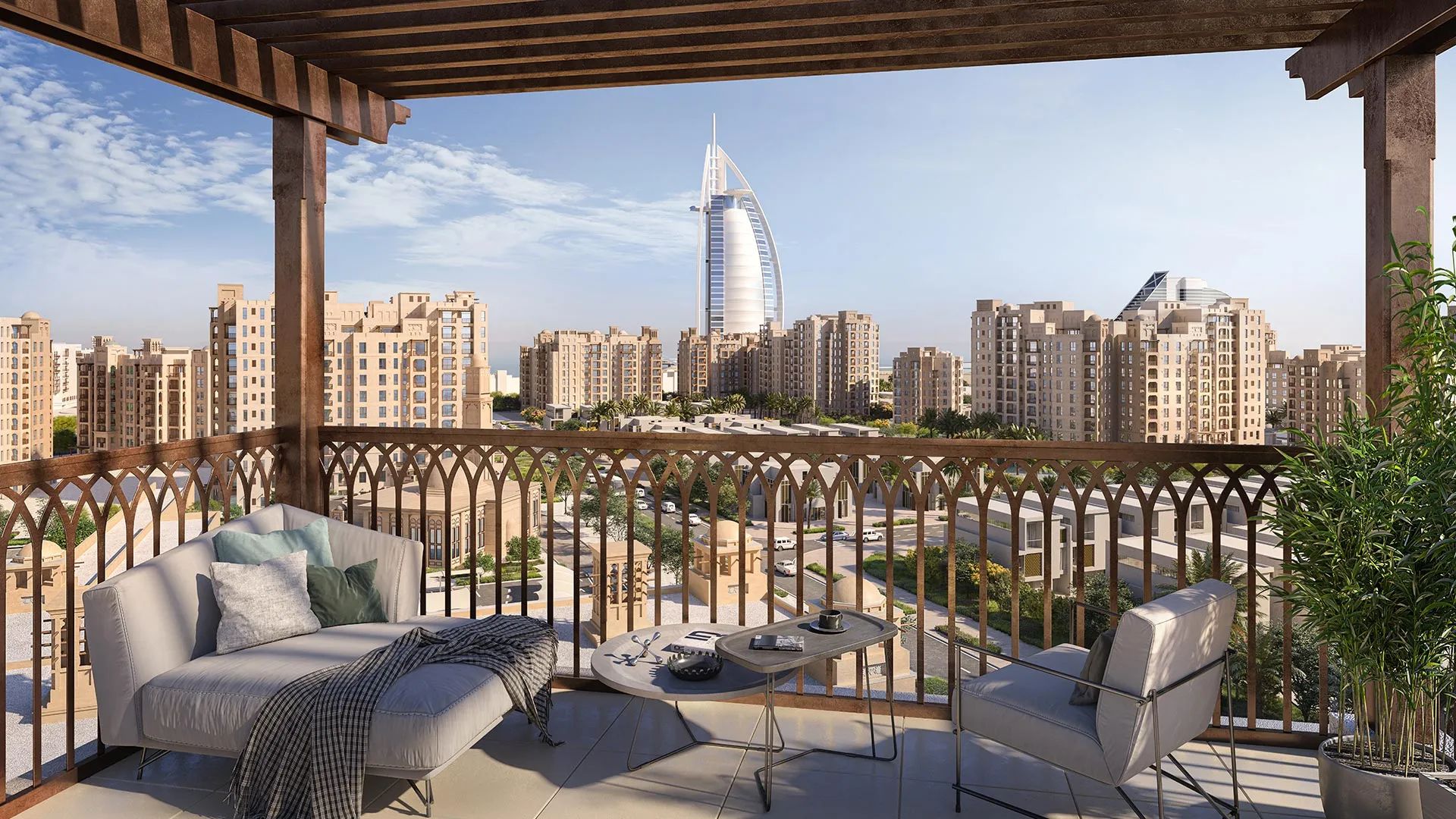 A balcony of Madinat Jumeirah with modern outdoor furniture overlooks a cityscape of beige buildings, featuring the iconic Burj Al Arab hotel in the distance under a clear blue sky.