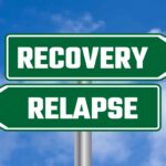 Two green directional signs against a blue sky with clouds; one points right and reads RECOVERY, the other points left and reads RELAPSE.