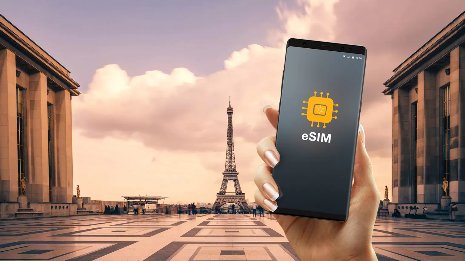 A hand holds a smartphone displaying an eSIM icon, with the Eiffel Tower and a large open plaza in Paris visible in the background under a partly cloudy sky.